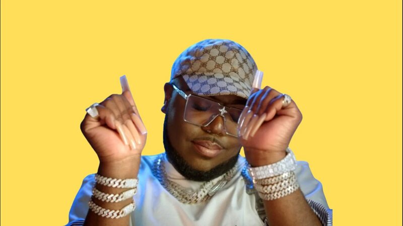 Portrait of Saucy Santana wearing a stylish outfit, designer cap, and jewelry, striking a confident pose against a yellow background.