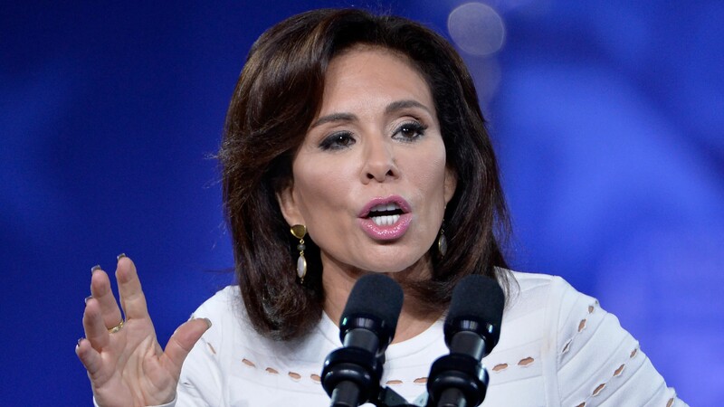 A woman speaking passionately at a podium with two microphones, wearing a white top, set against a blurred blue background.