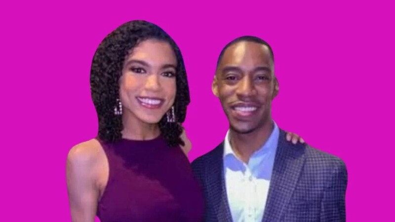 Smiling couple posing against a bright pink background, with the woman wearing a sleeveless maroon dress and the man in a blue shirt and checkered blazer.